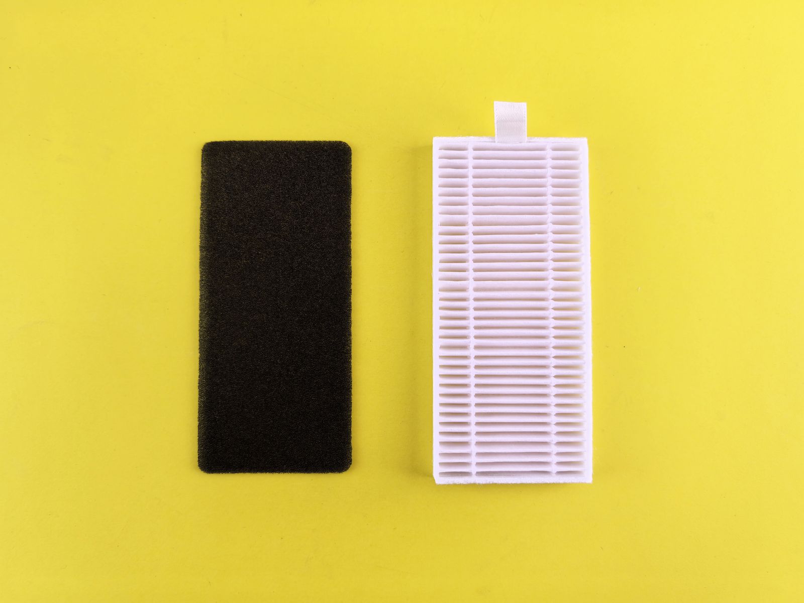 A white pleated air filter beside a black foam filter.