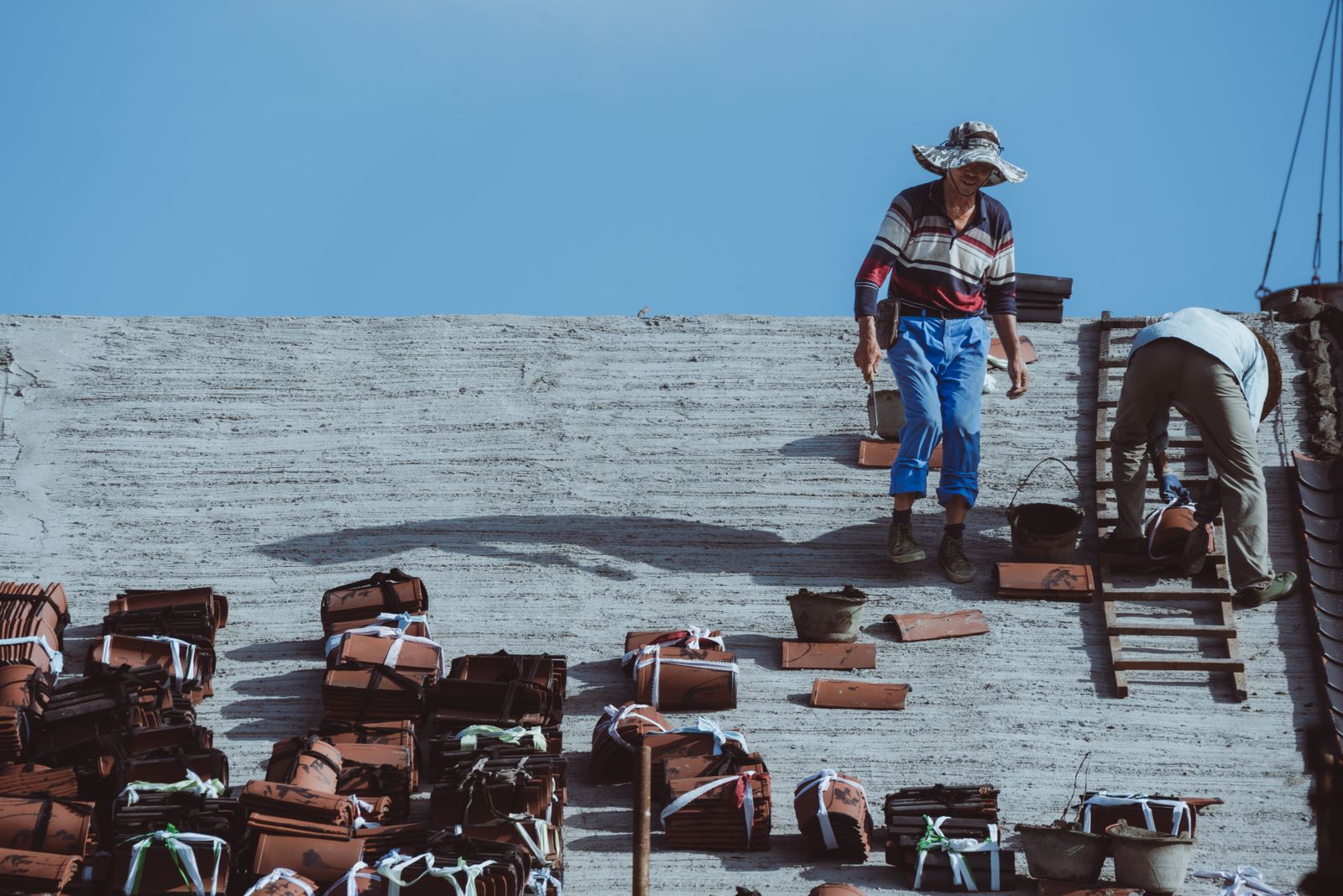 Roof installers placing tiles across a residential roof.
