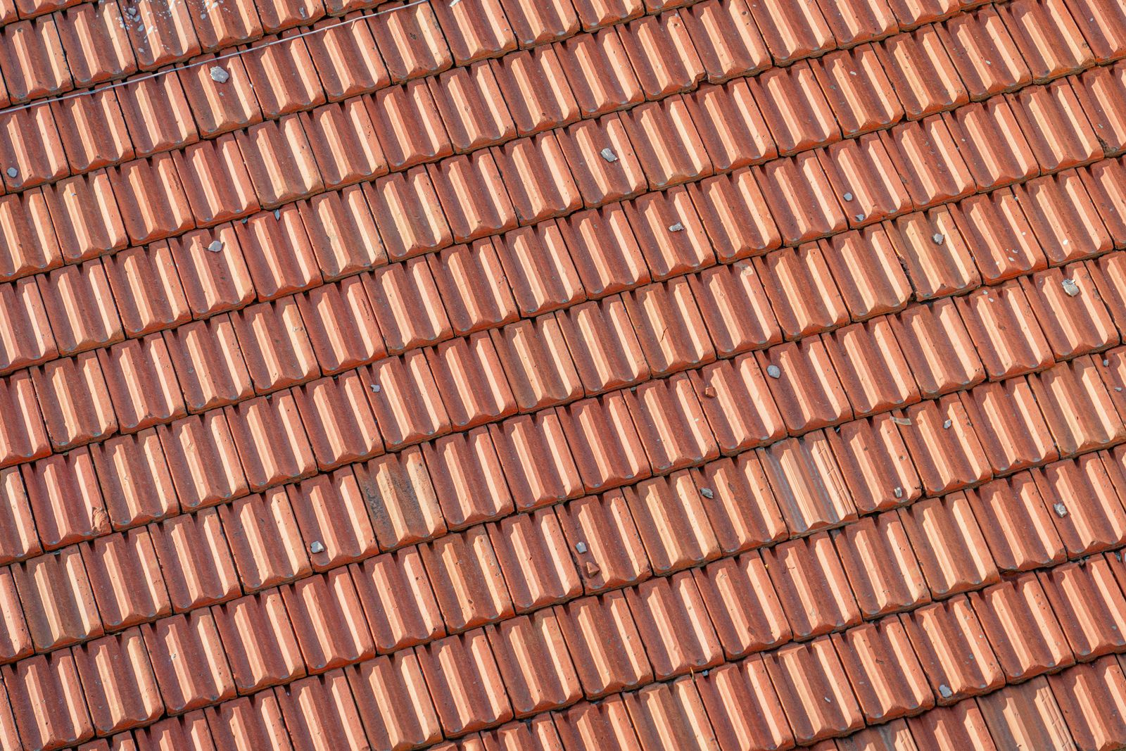 Overlapping red clay roof shingles in close detail.