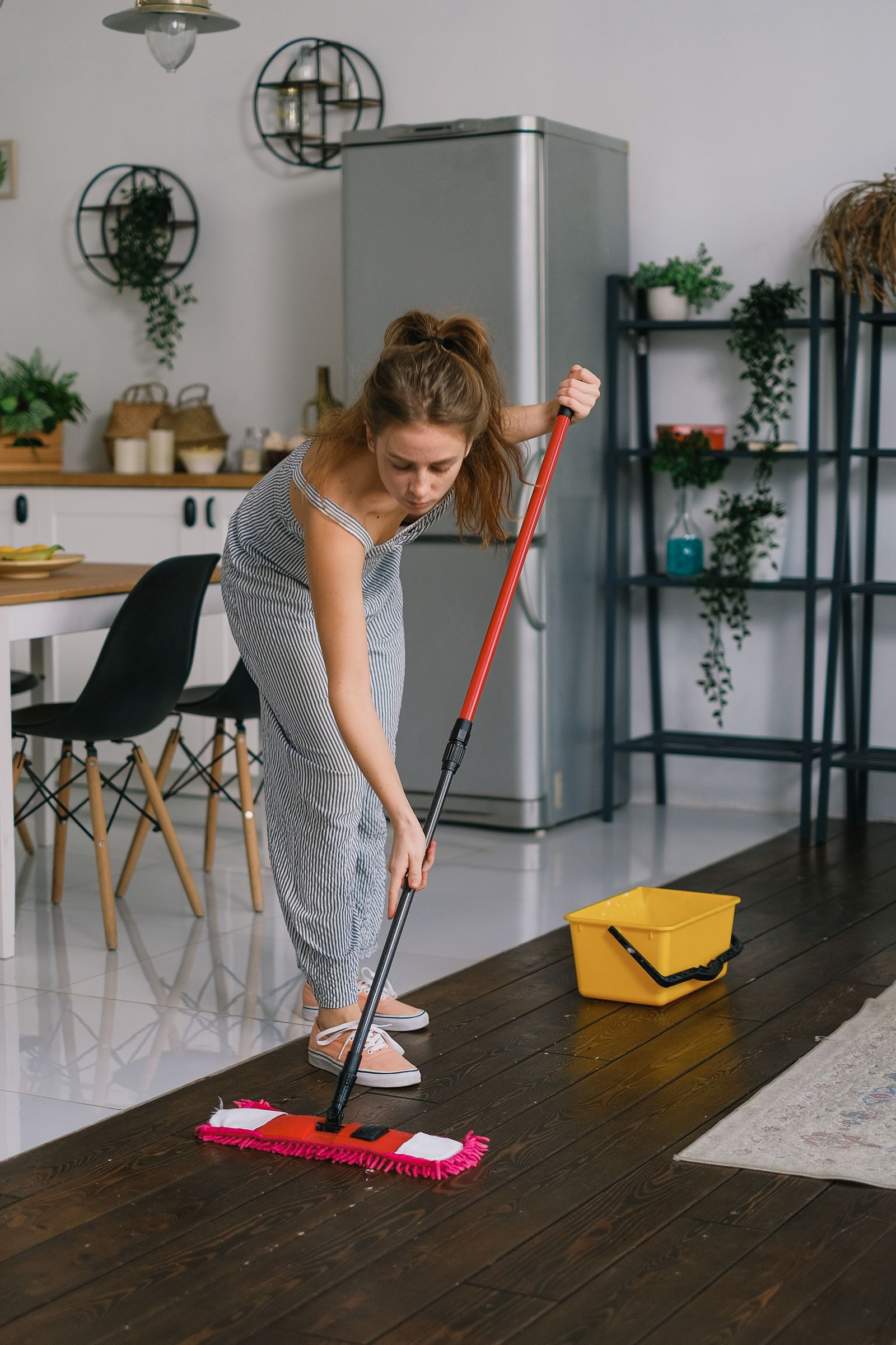 A person using a mop and bucket to clean a wooden kitchen floor.